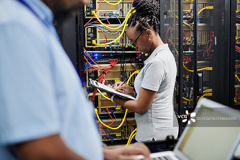 年轻女子在服务器机房工作并手持写字板图片素材