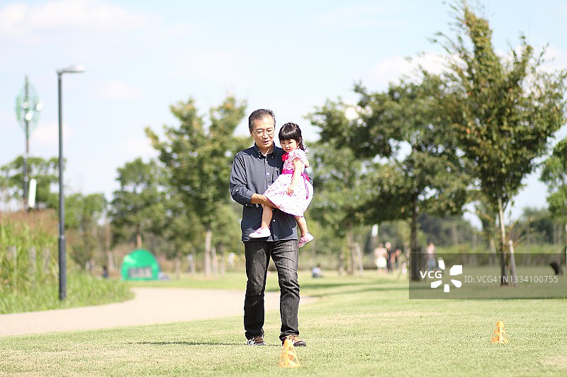 穿着派对礼服的孩子被父亲抱着在草地上行走图片素材