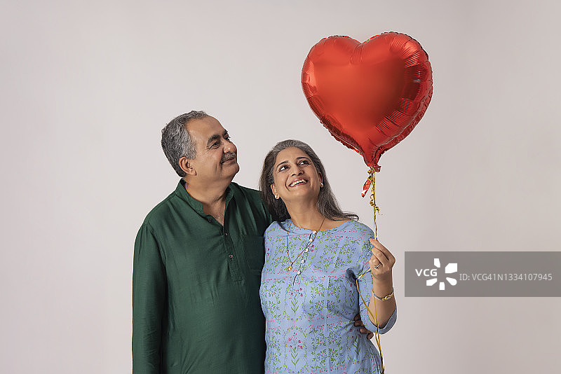 一对快乐的成年夫妇站在一起，手持爱心气球图片素材