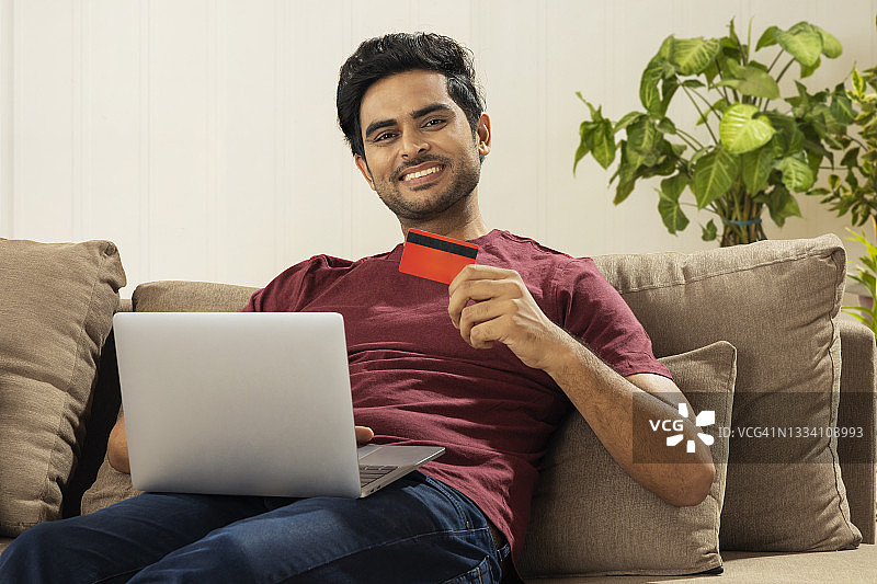 坐在家里进行在线交易的快乐年轻男子图片素材