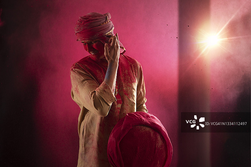 身上沾满洒红节色彩，弯腰摸耳朵的年轻男人图片素材