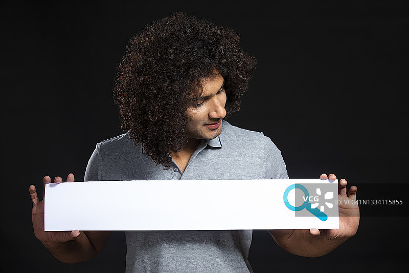 拿着搜索栏并看着它的卷发年轻人图片素材