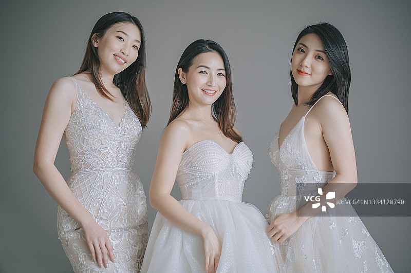 新娘和伴娘在灰色墙前看向镜头微笑图片素材