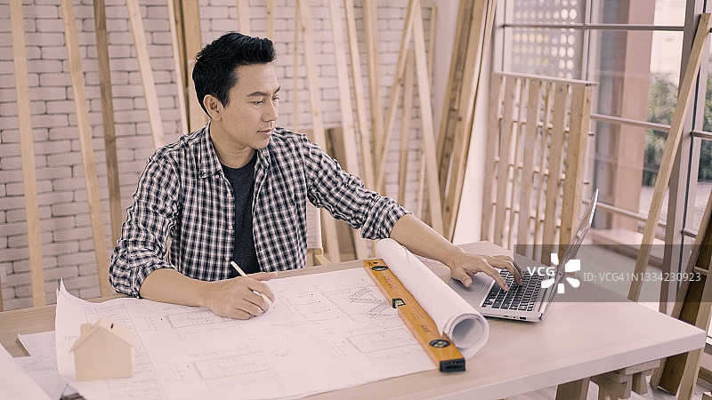 男人在车间里一边用笔记本电脑一边画图图片素材