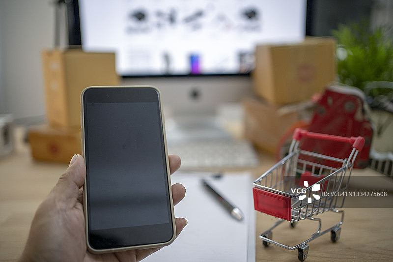 手拿手机和迷你购物车，在线购物图片素材