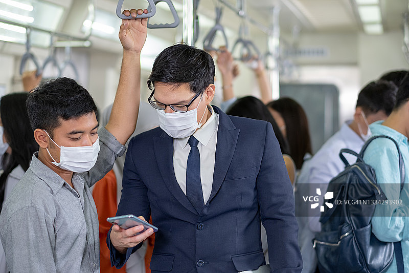 戴着口罩的亚洲商人看手机，与朋友乘坐地铁上班图片素材
