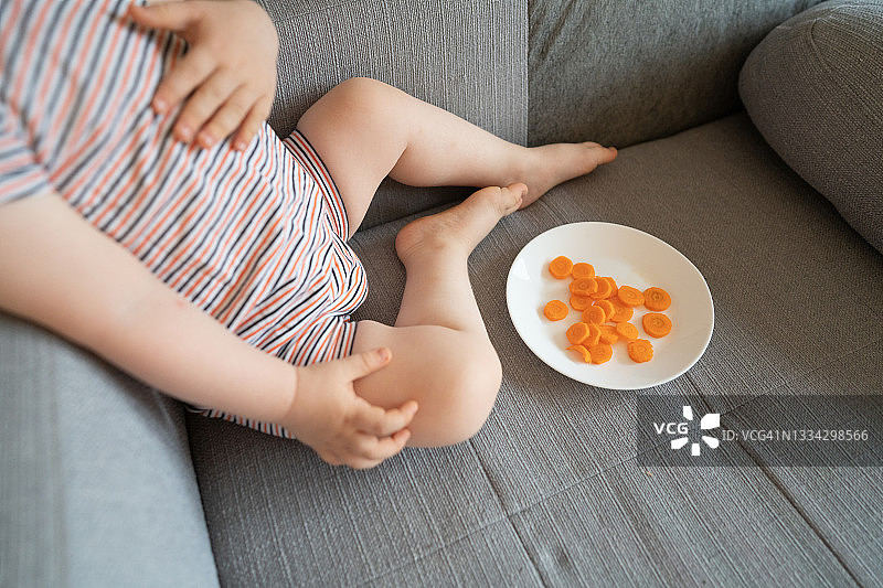 坐在沙发上吃胡萝卜的男婴图片素材