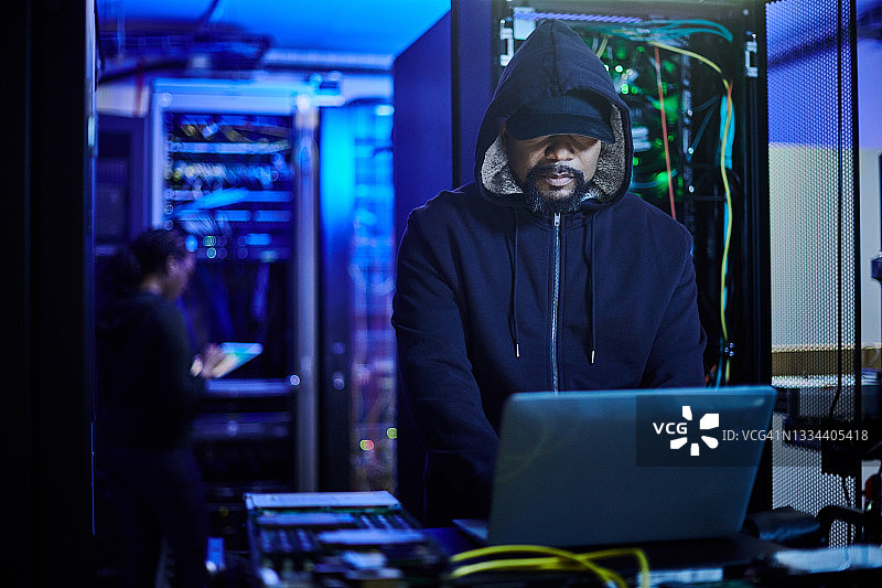 年轻男程序员站在黑暗服务器机房使用笔记本电脑照片图片素材
