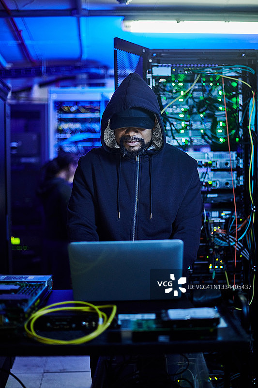 年轻男程序员站在黑暗服务器机房使用笔记本电脑照片图片素材