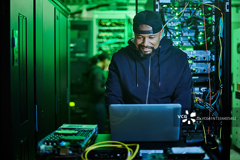 年轻男程序员站在黑暗服务器机房使用笔记本电脑照片图片素材