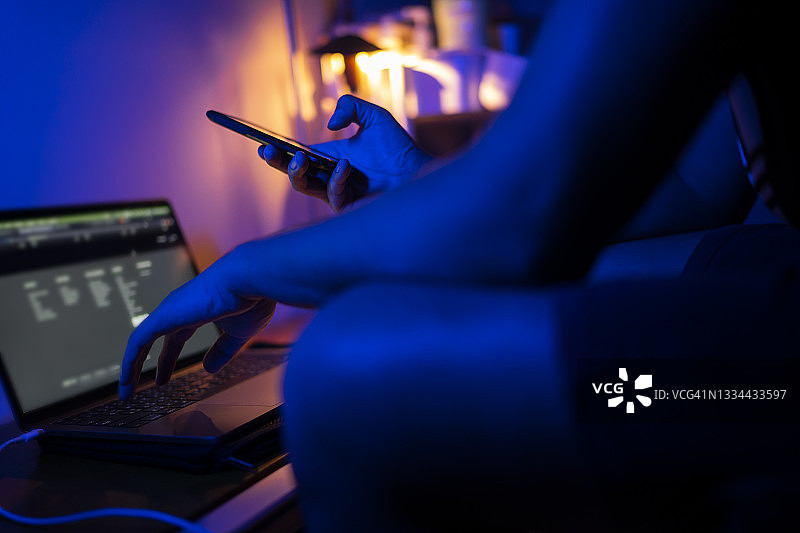 在卧室里使用手机和笔记本电脑的年轻人，背景色彩鲜艳图片素材