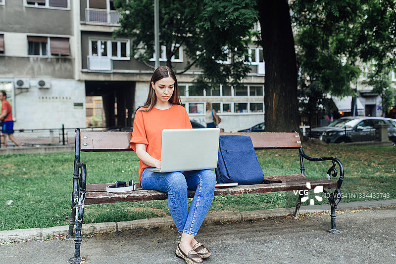 坐在长椅上使用笔记本电脑的年轻女人图片素材