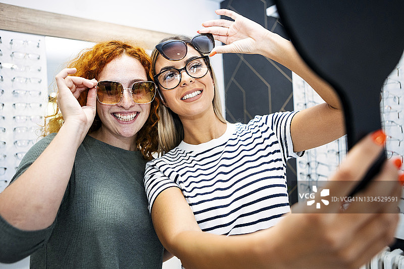 年轻女子在眼镜店试戴眼镜，看着镜子图片素材
