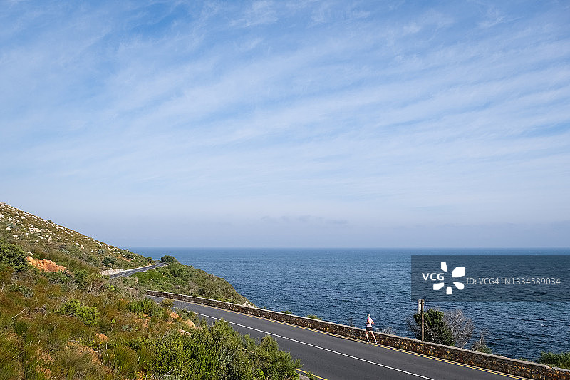 健康的跑步女运动员沿着海滨公路奔跑，欣赏海景图片素材