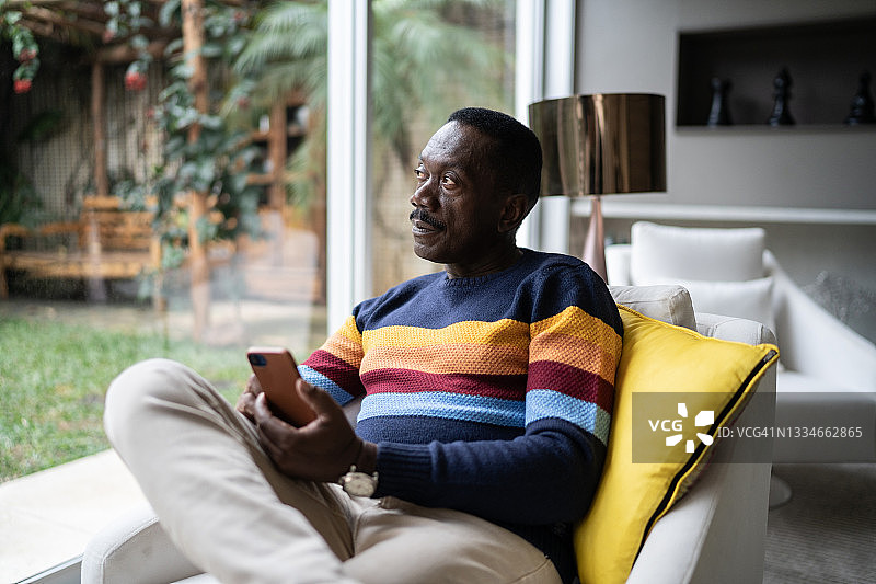 年长的男人在家沉思并使用智能手机图片素材