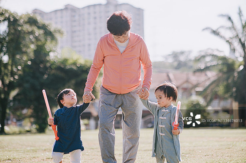 亚洲祖母牵着双胞胎孙子的手在公园里散步图片素材