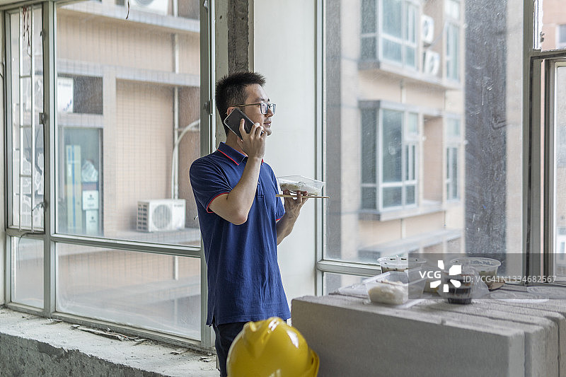 在施工现场打电话吃外卖的亚洲男工程师图片素材