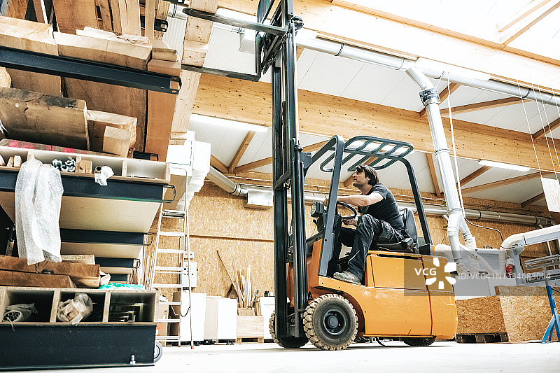 在木工制造车间，工人用叉车在储物架前工作图片素材