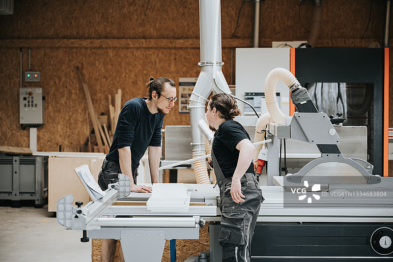 两个年轻的木匠在车间圆锯机旁交谈图片素材