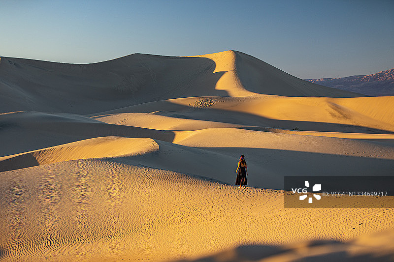 女子身穿连衣裙站在广阔的金色沙丘中央图片素材