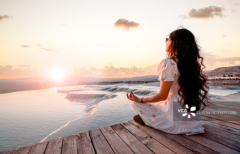 美丽的女人在帕穆克卡莱的石灰华池日落时分冥想，双手呈莲花式做瑜伽图片素材