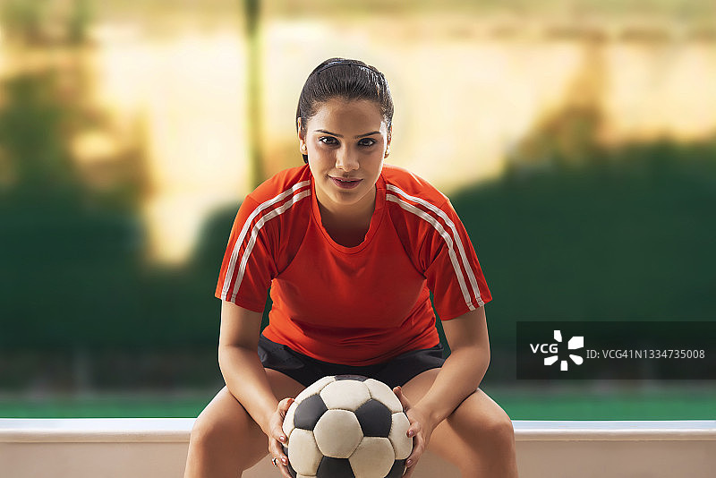 开心的女球员抱着足球坐着图片素材