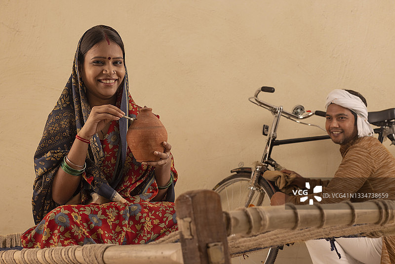 乡村妇女看着镜头，与丈夫一起将钱存入存钱罐图片素材