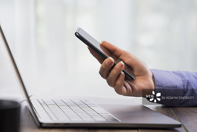手在手机上工作，前方有一台笔记本电脑图片素材