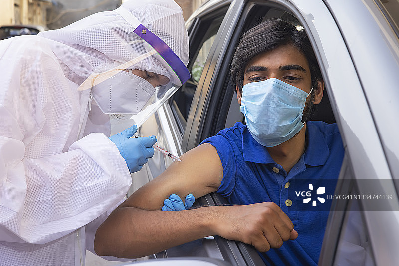 身穿防护装备的医护人员为一名在车内的男子接种新冠疫苗图片素材