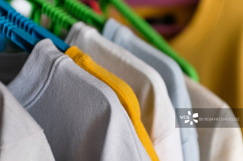 衣服挂在设计师服装店的架子上，干净熨烫的衣物，纺织T恤挂在更衣室的衣架上，在家里，在室内。家务、熨烫、护理和存放的概念。女士衣橱。图片素材