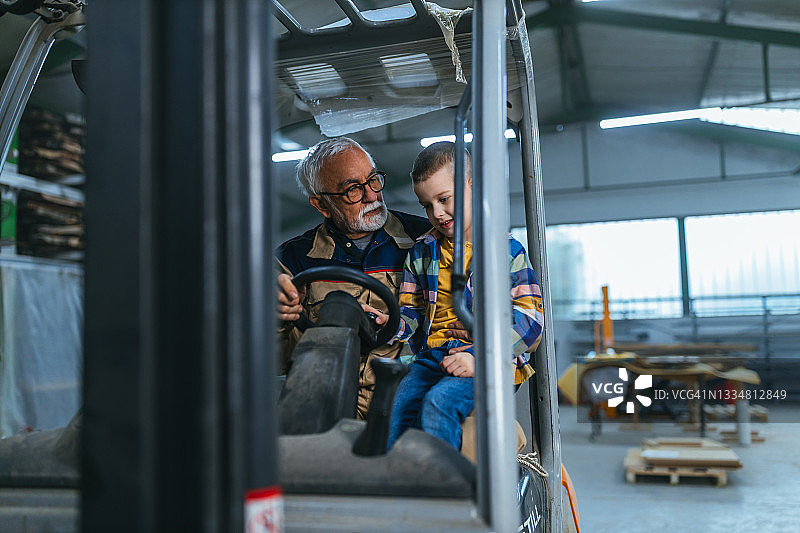 仓库工人向孙子展示叉车的工作原理图片素材