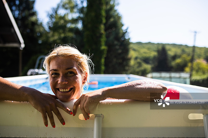 一位年轻漂亮的女子靠在地上游泳池的边缘微笑图片素材
