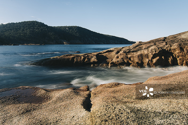 塔斯马尼亚沉睡湾，橙色岩石和山脉环绕的蓝色海洋图片素材