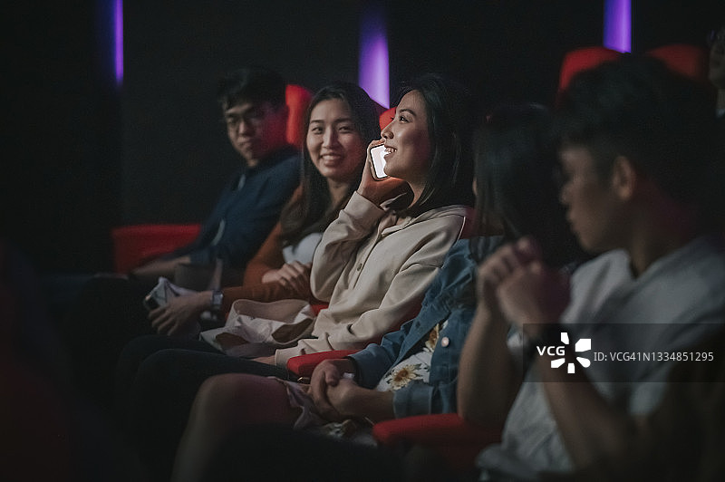 在电影院黑暗中讲电话的亚洲女人，打扰其他观众图片素材
