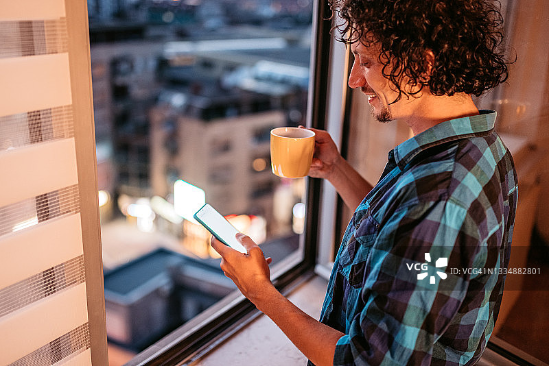 在窗台边喝咖啡并查看手机社交媒体的男人图片素材