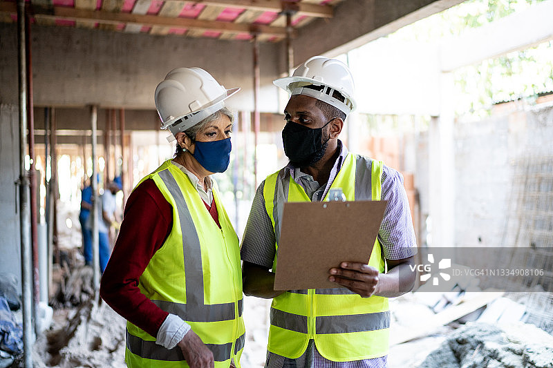 在建筑工地上进行非正式会议的工程师和承包商，戴着防护面罩图片素材