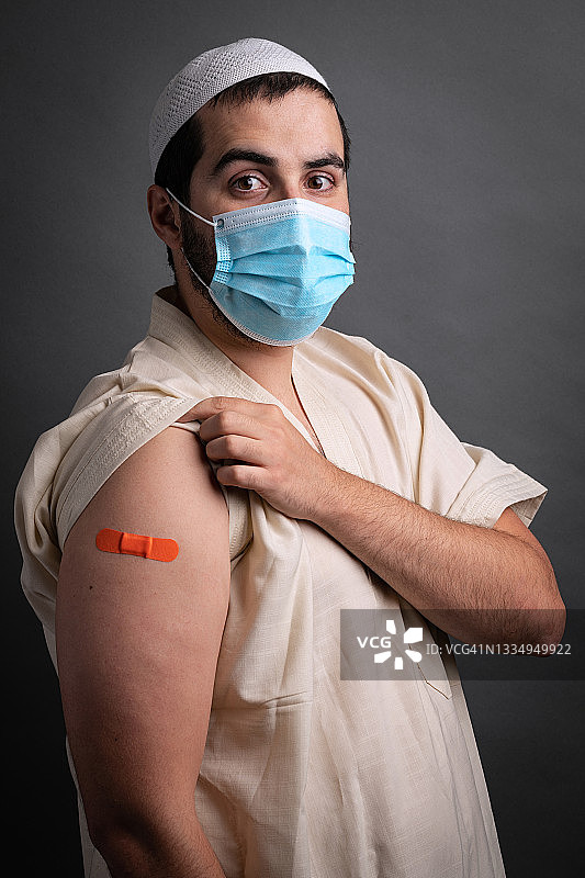 年轻的穆斯林男子展示手臂上的疫苗接种创可贴图片素材