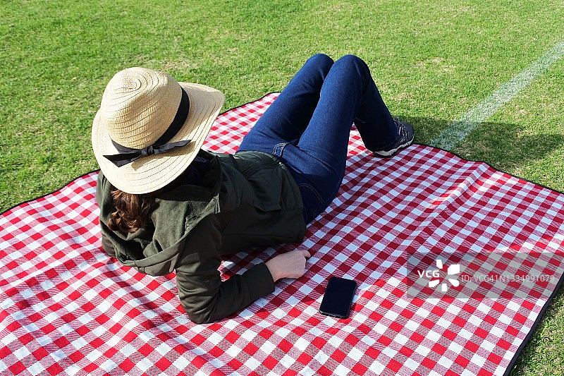 女人坐在野餐垫上，旁边放着手机图片素材