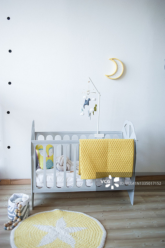 婴儿房：灰色木床、黄色格子布、彩色飞龙挂饰、月亮灯、星星针织地毯图片素材