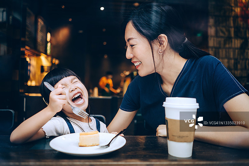 年轻的亚洲母亲和可爱的女儿在咖啡馆分享芝士蛋糕图片素材