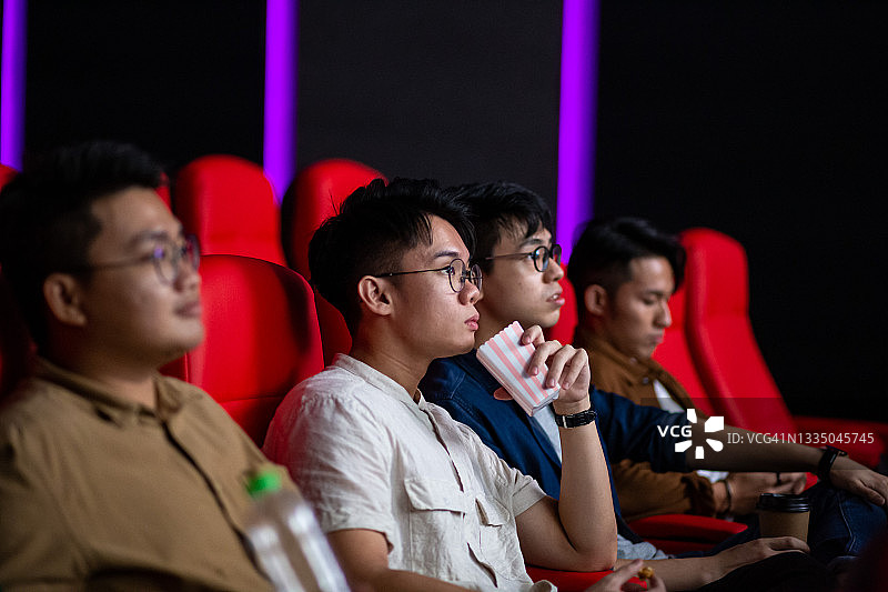 一群亚洲年轻男人在电影院里观看电影，欢笑不已图片素材
