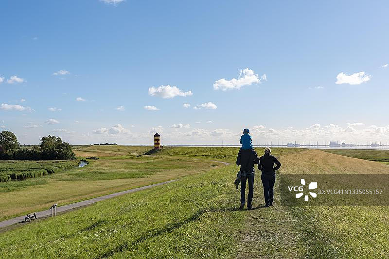 年轻家庭在德国下萨克森州皮尔苏姆灯塔附近的高水位水坝上行走图片素材