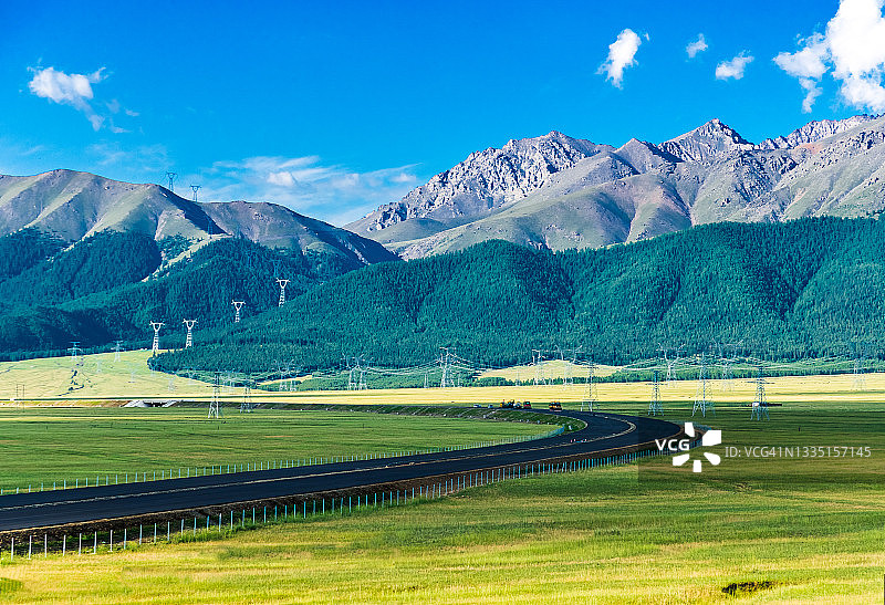 天山脚下的牧场，绿油油的草原。高压输电线路和输电塔沿着山脉一直延伸到远方。中国新疆维吾尔自治区。图片素材