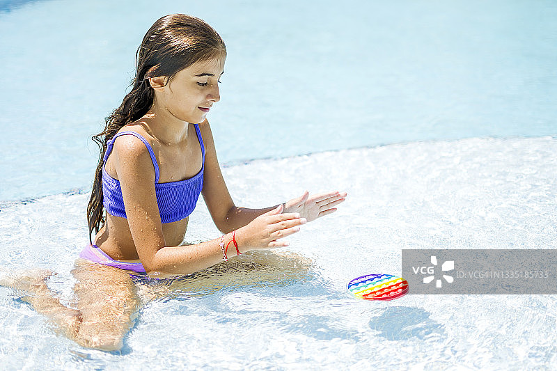 在游泳池边玩彩虹按按乐的漂亮女孩图片素材