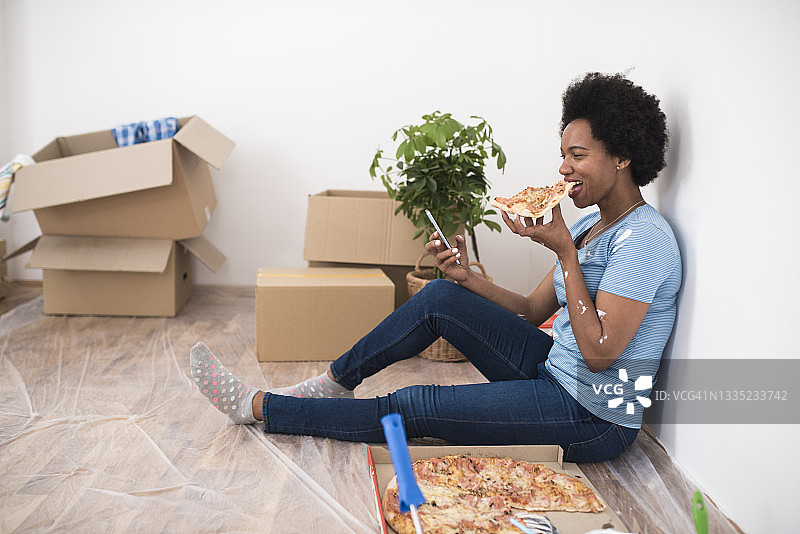 装修公寓时休息吃披萨的非裔美国妇女图片素材