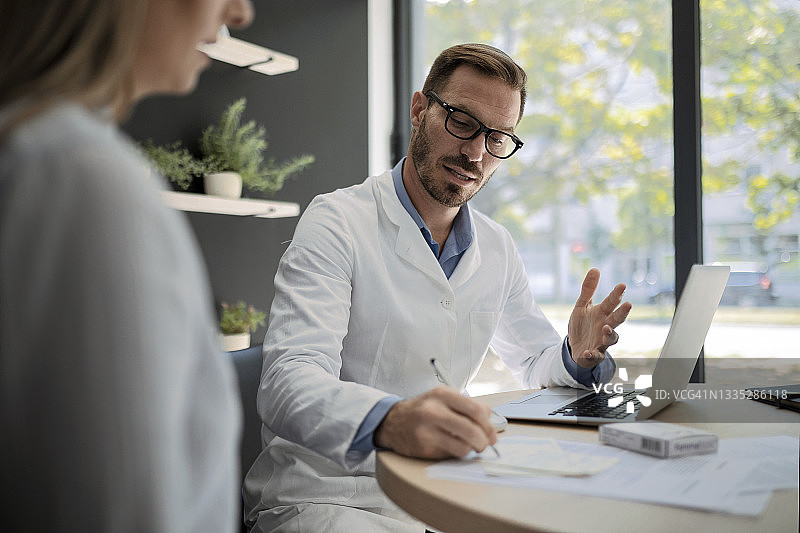 男医生在办公室用笔记本电脑为病人开处方图片素材