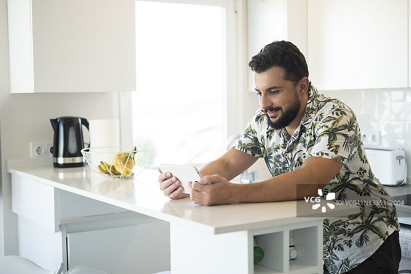 快乐的胡子男在家中厨房看平板电脑图片素材