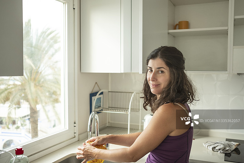 穿着休闲运动装的女人在洗碗，对着镜头微笑图片素材