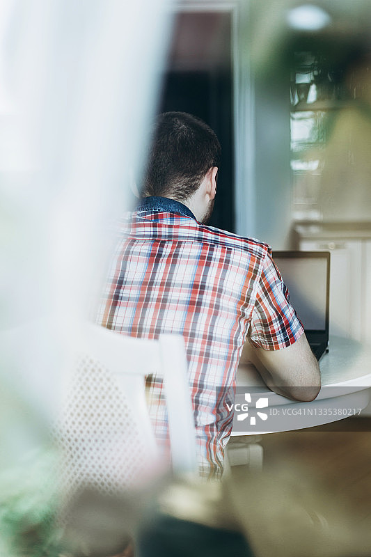 穿着格子衬衫的年轻男人坐在笔记本电脑前图片素材
