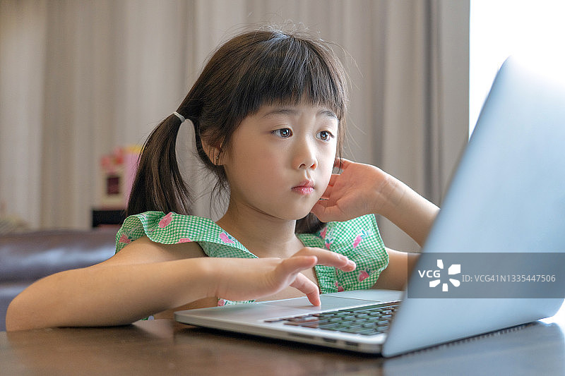 儿童在线教育。小女孩在家使用笔记本电脑。图片素材
